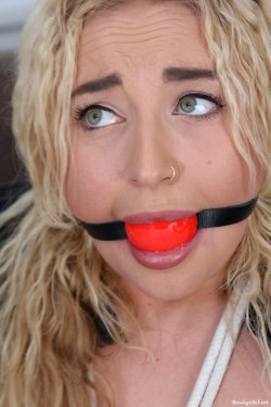 close up of zoey zipties face with a red ball gagged strapped into her mouth